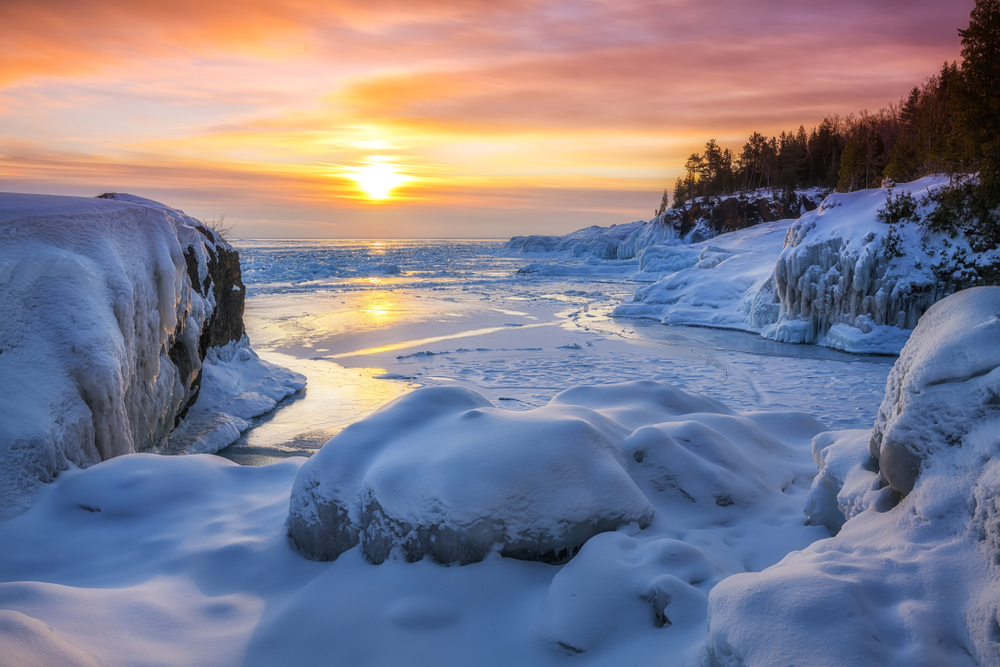 In Marquette, which is one of the Best Destinations For A Magical White Christmas In The USA, the coast and rocks are filled with ice and snow, Lake Superior beginning to freeze as the sun dips.