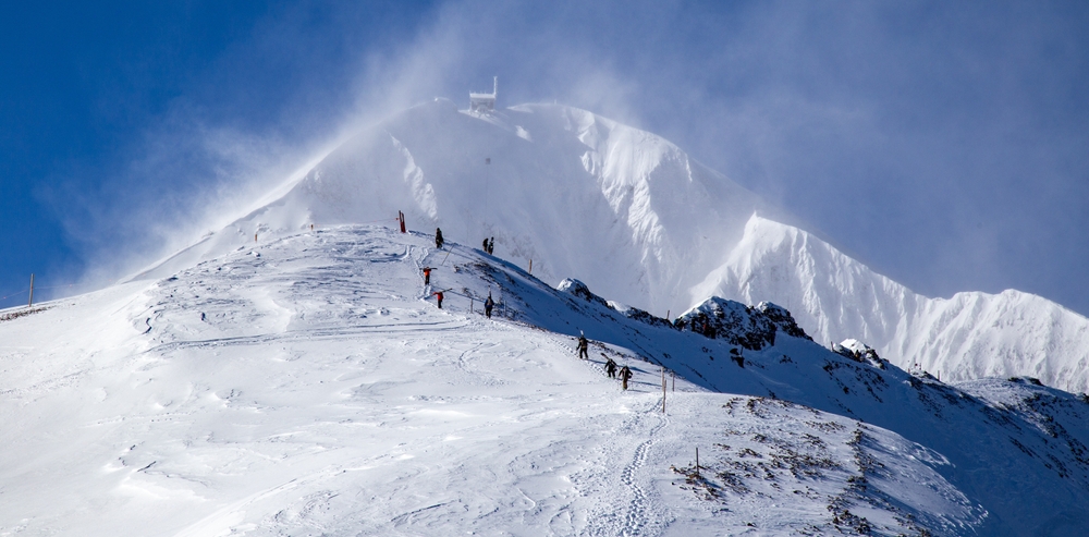In Big Sky, Montana, which is one of the Best Destinations For A Magical White Christmas In The USA, guests ski down a mountain that is covered in white powder, the snow floating in the air.