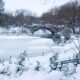 In Park City, which is one of the Best Destinations For A Magical White Christmas In The USA, a little park with benches, a lake and bridge are covered in snow.