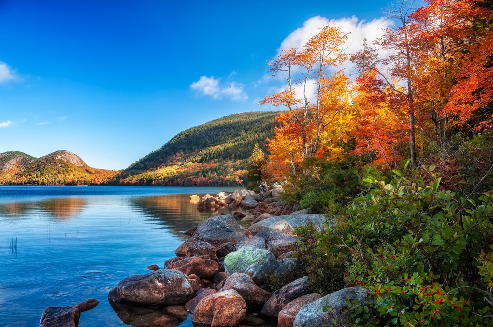 In Maine a lake is pristine and calm with rocky shores and fall foliage all around.
