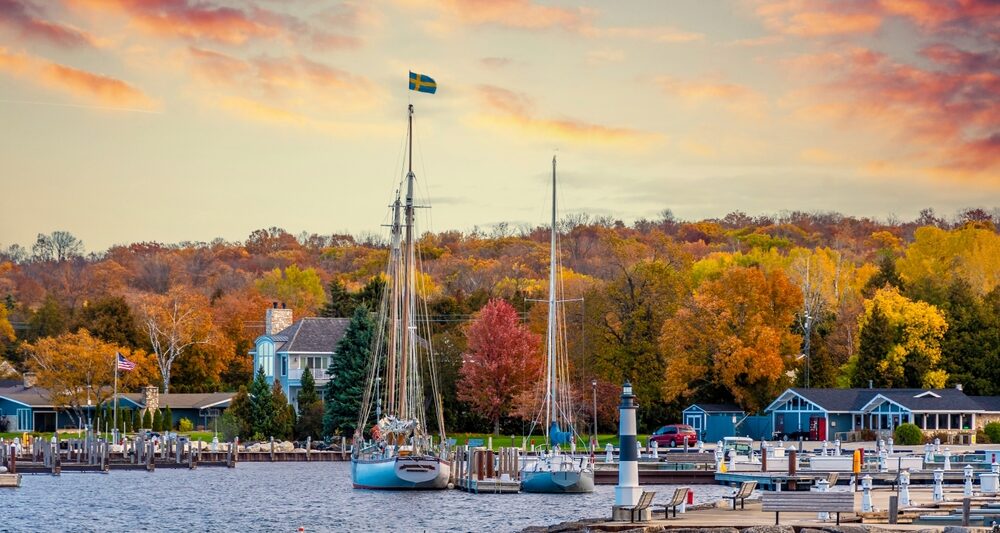 In Wisconsin, one of the Best States for Fall Foliage in the USA, boats sit on a lake at sunset, with tons of fall foliage in the backdrop.