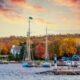 In Wisconsin, one of the Best States for Fall Foliage in the USA, boats sit on a lake at sunset, with tons of fall foliage in the backdrop.