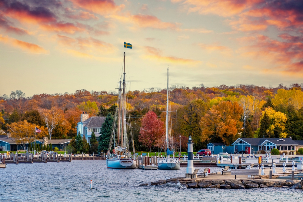 IN Wisconsin boats dock on the coast during sunset, with all the trees beyond them turning red and orange and yellow.