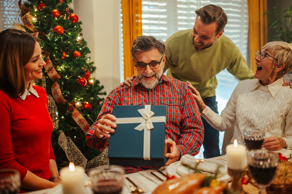 A family laughs at one another, enjoying Christmas time at the dinner table while opening presents.