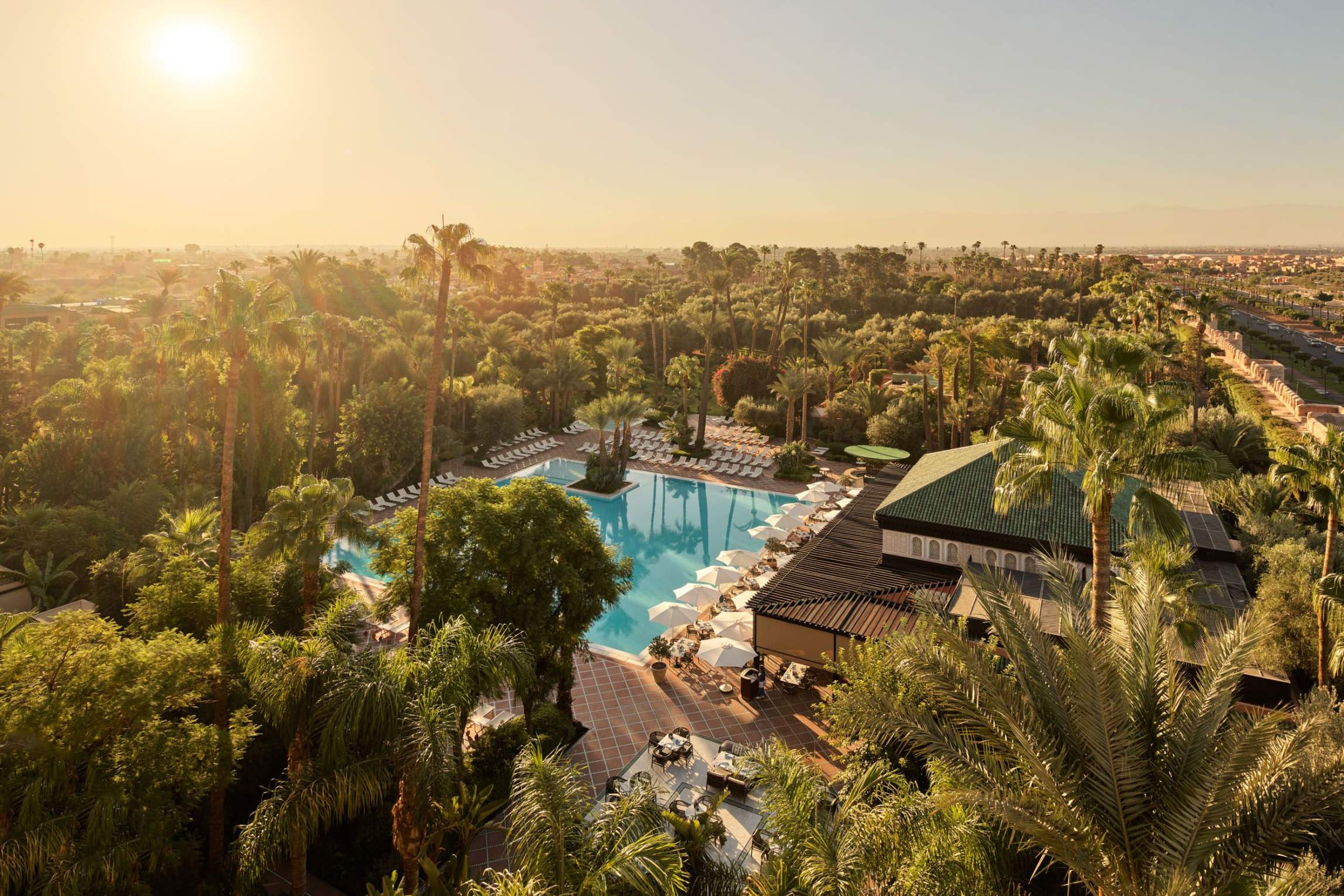 An overhead shot shows La Mamounia in Morocco which is one of the 10 Most Luxurious Hotels to Spend Christmas Around the World, and it features a huge pool with tons of palm trees.