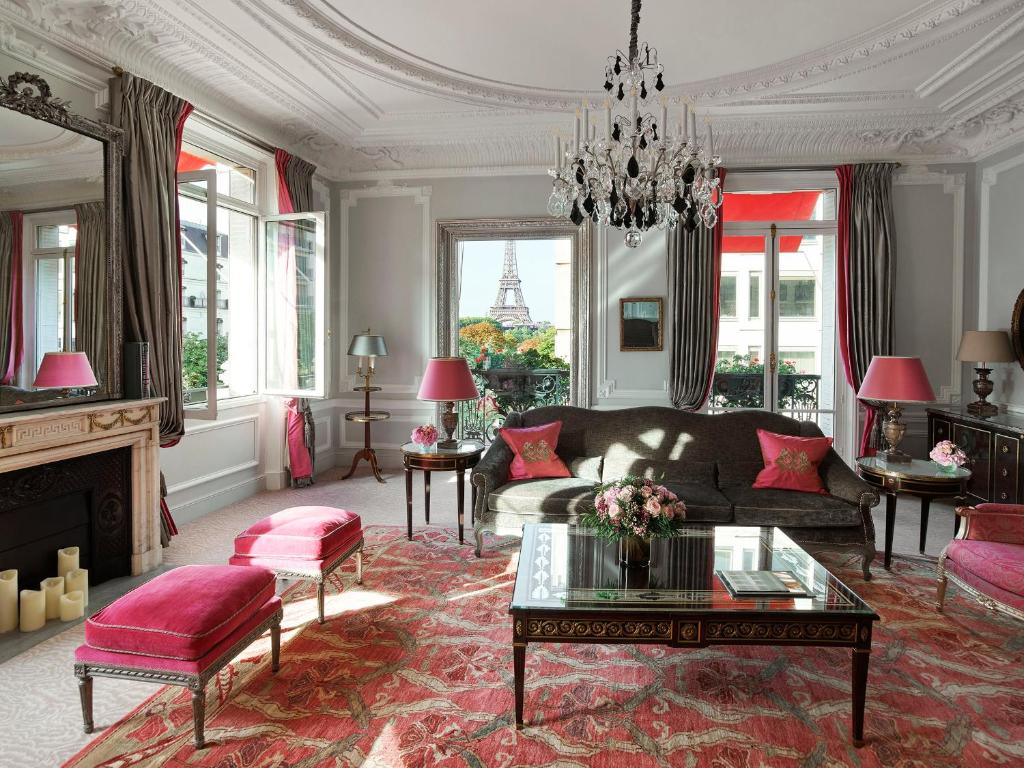 A paris luxury hotel features red designs with couches, fireplaces, and more near a terrace that overlooks the Eiffel tower.