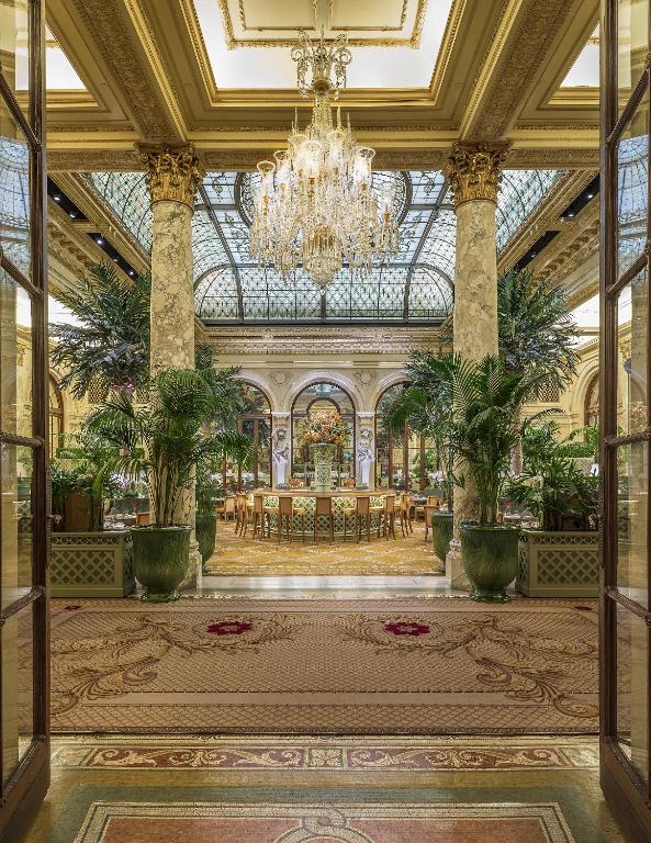 The entry way of this hotel features a stunning walk through with plants, dining seating and ornate decor.
