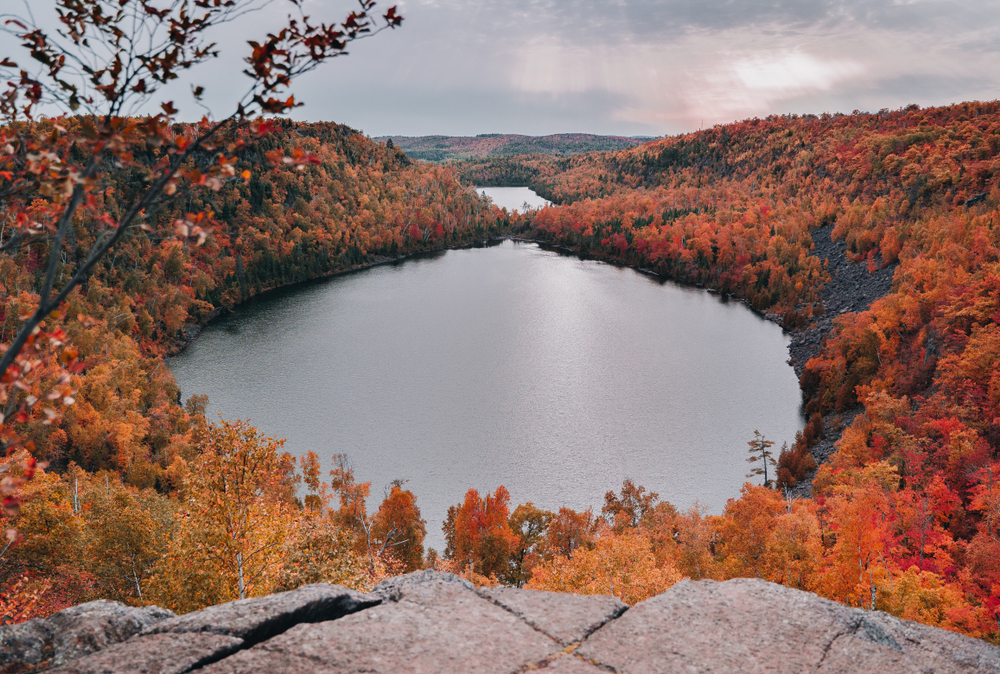 An overhead shot of Lake Superior shows the lake from a viewpoint, with trees turning red and orange around it.