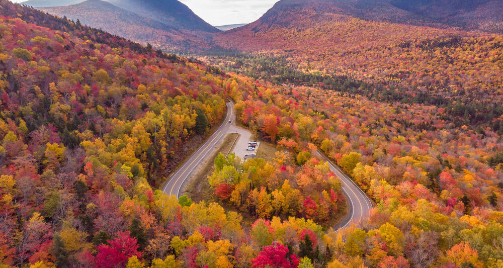 A loop in New Hampshire shows a road, which is one of the Most Scenic Fall Drives in the USA, that skirts through trees turning colors.