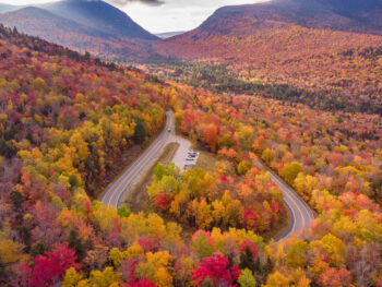 A loop in New Hampshire shows a road, which is one of the Most Scenic Fall Drives in the USA, that skirts through trees turning colors.