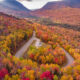 A loop in New Hampshire shows a road, which is one of the Most Scenic Fall Drives in the USA, that skirts through trees turning colors.
