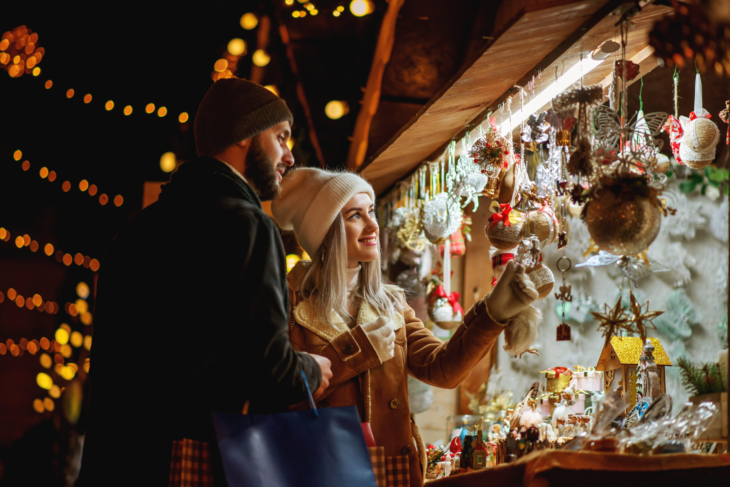 Happy smiling couple shopping at Christmas street market, choosing gifts.