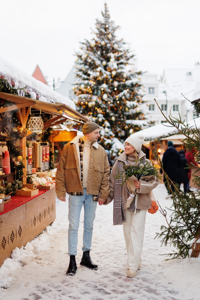 Beautiful couple with bouquet walking at the christmas market. The article is about Christmas market trip to Europe.