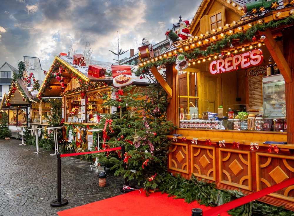 Festive Christmas market in Hamburg, Germany, with decorated stalls, holiday lights, and a crepe stand. The article is about Christmas market trip to Europe.