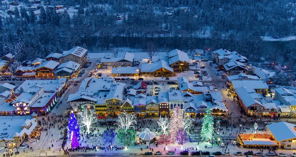 an ariel view of the town of Leavenworth with Christmas lights ice staking rink and snow covered streets the trees in the foreground are multicolored and this is one of the Best christmas vacations in the USA