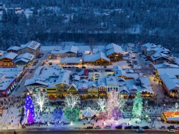 an ariel view of the town of Leavenworth with Christmas lights ice staking rink and snow covered streets the trees in the foreground are multicolored and this is one of the Best christmas vacations in the USA