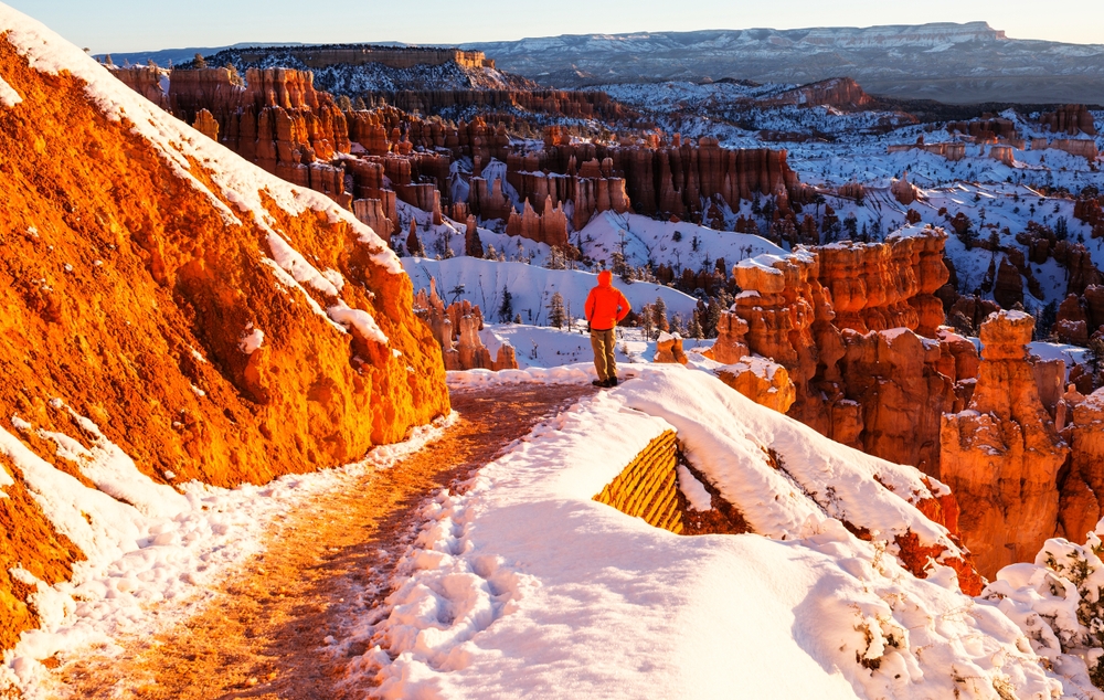christmas time in the USA in Bryce Canyon with dusting of snow on the red rocks as a man in red jacket stands at a lookout point Best christmas vacations in the USA for outdoor lovers