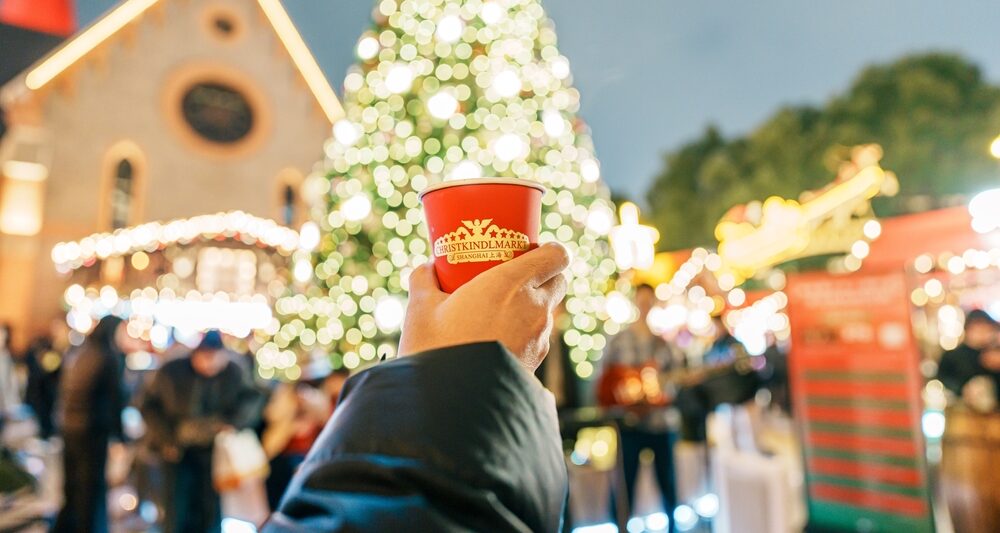 girl holding a cup in front of a christmas tree at one of the Christmas Markets in Europe