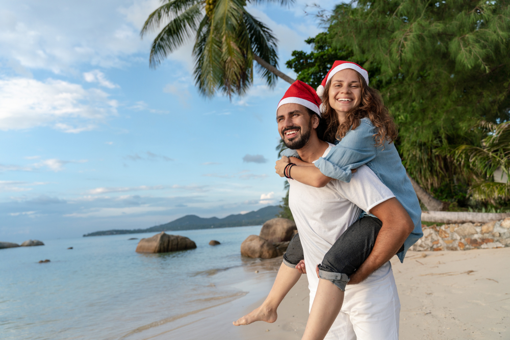 a couple with Christmas hats standing on a beach with palm trees in Hawaii