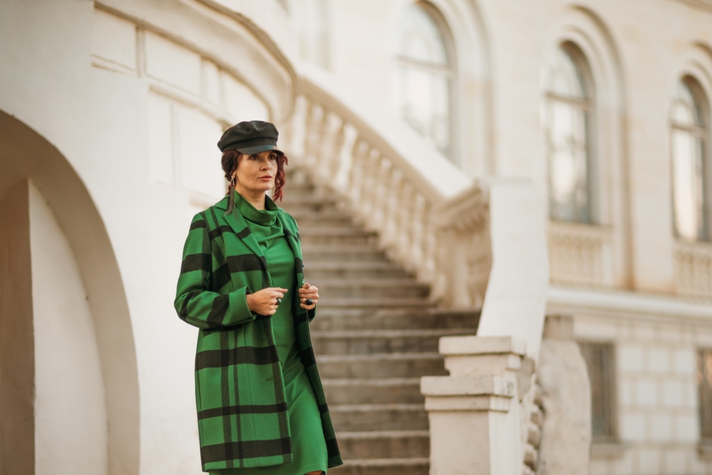 A woman climbs down a set of stairs in a long green dress, with a wool green jacket, and a beret: she knows what to wear in Europe in winter and wears it with fashion.