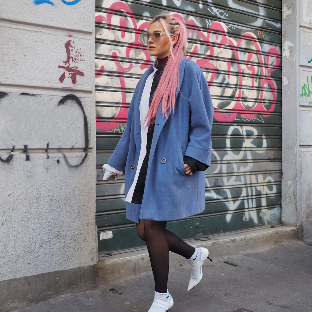 A woman knows What to Wear in Italy in fall where she channels fashion and comfort in tights and a wool jacket with her pink hair.