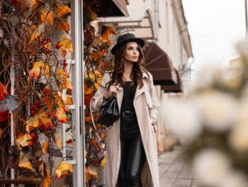 A woman walks down the street, fall leaves turning, in her trench coat, leather pants and hat, knowing full well What to Wear in Italy in fall.