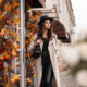A woman walks down the street, fall leaves turning, in her trench coat, leather pants and hat, knowing full well What to Wear in Italy in fall.