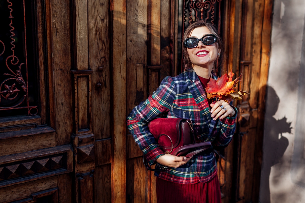A woman knows What to Wear in Italy in fall as she poses against a wooden door to match her style with a plaid blazer and thick pants.