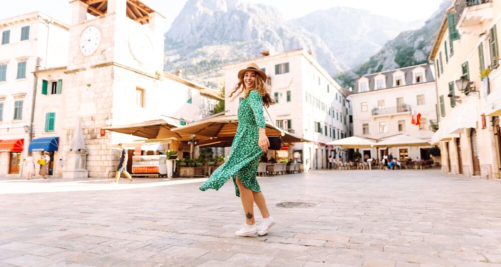 A woman turns in a city square, wearing a green floral dress and white shoes, knowing What to wear in Italy in spring.