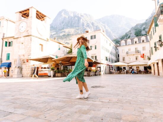 A woman turns in a city square, wearing a green floral dress and white shoes, knowing What to wear in Italy in spring.