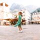 A woman turns in a city square, wearing a green floral dress and white shoes, knowing What to wear in Italy in spring.