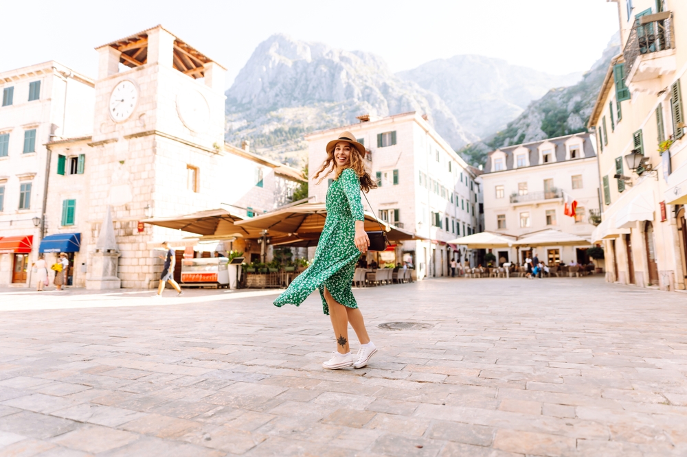 A woman spins in a city square, wearing white shoes and a floral dress and hat, so ready for spring.