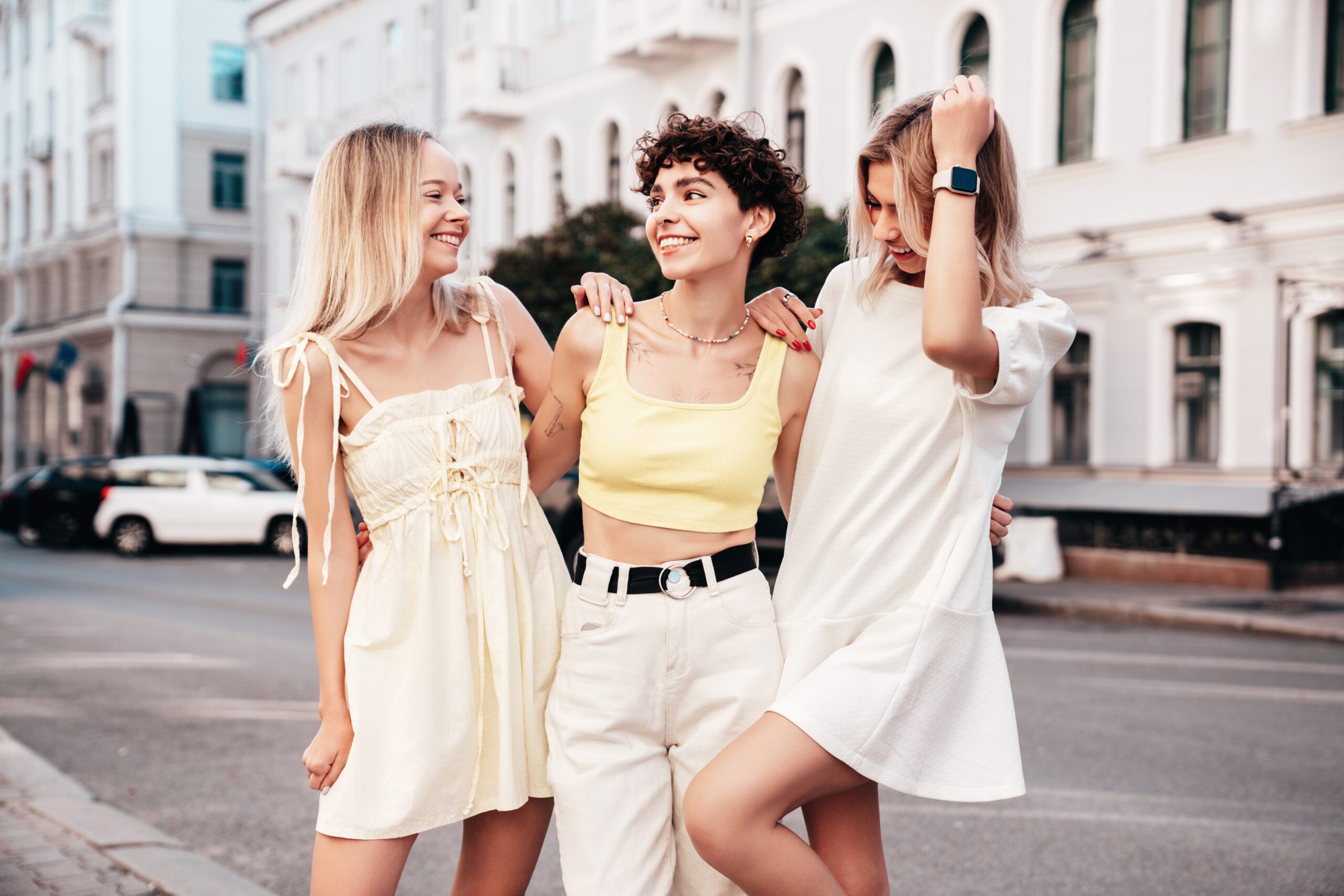 Three friends pose on the street in dresses, tanks and pants, enjoying the warmth of spring.