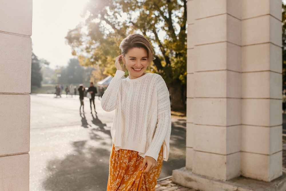 A woman smiles at the camera while wearing a maxi dress with a sweater over it: perfect for spring!