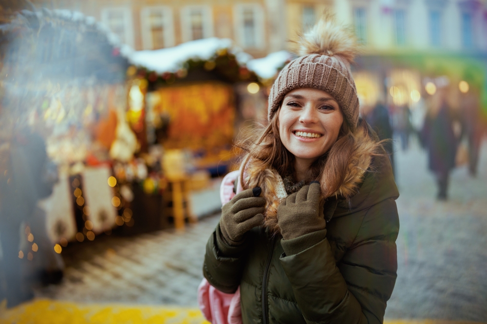 A woman smiles while exploring the Christmas markets, knowing what to wear in Italy in winter in her olive parka and beanie.