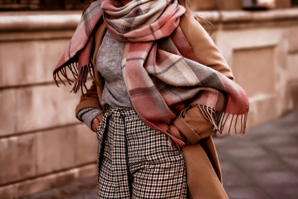 A close up shot shows an individual sticking their hands in their wool pants with their wool shirt and their trench coat and scarf on.