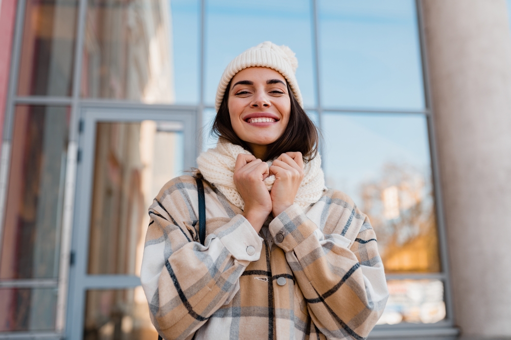 A woman grasps at her knit scarf that lays over her heavy flannel and matches her beanie: she knows what to wear in Italy in winter.