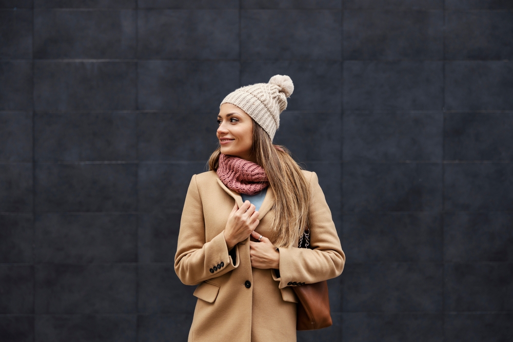 A woman closes her wool peacoat around her as she looks over her shoulder, her beanie and scarf showing she knows what to wear in Italy in winter to keep warm!