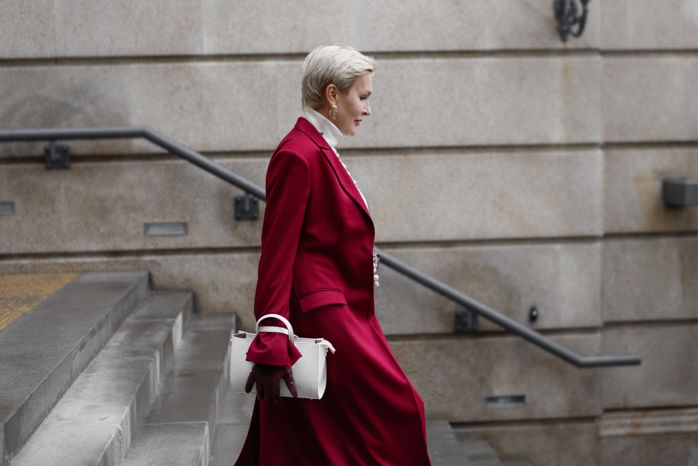 A woman walks down stairs, knnoinwg what to wear in Italy in winter and making a fashion statement in her red coat, turtleneck, and leather gloves.