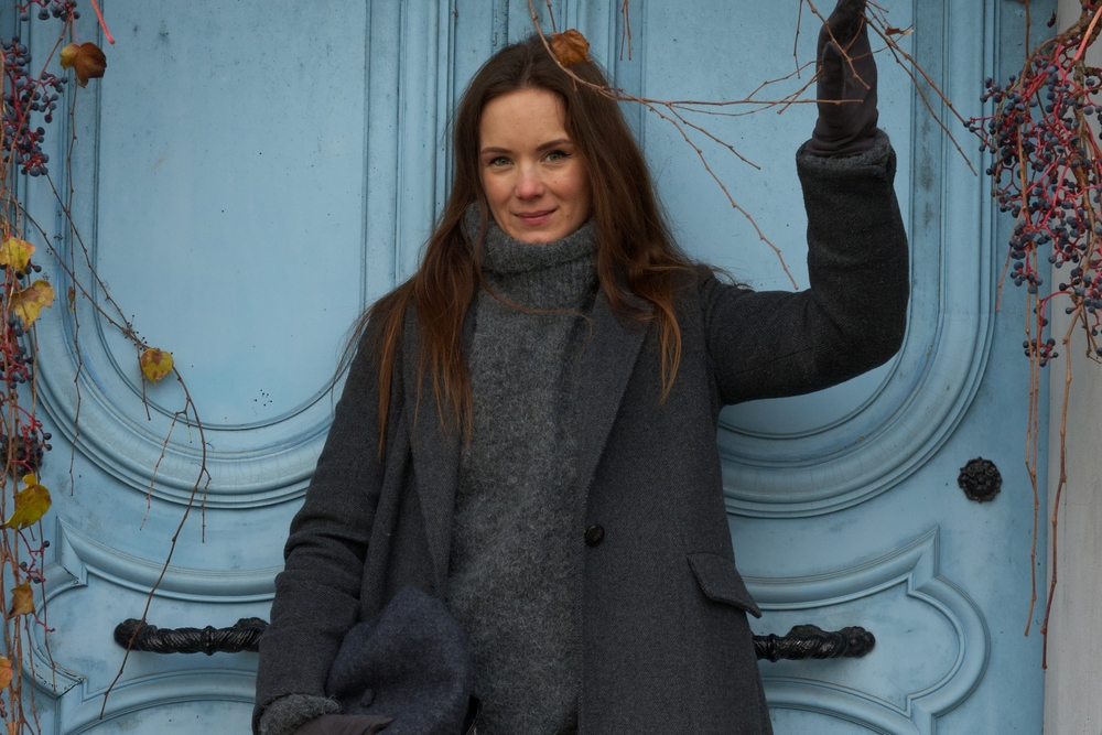A woman channels her inner wool look with a wool turtleneck and peacoat as she stands in front of a blue doorway.