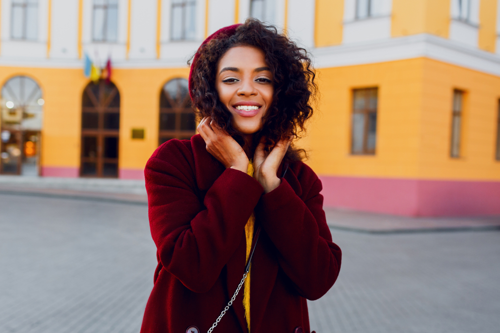 A close up of a woman shows her pulling her fleece jacket hood up over her head in the cool weather: her yellow sweater under the fleece jacket shows she knows what to wear in Italy in winter.