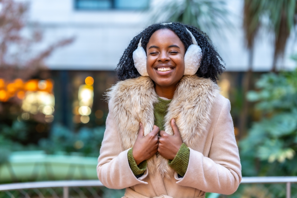 A woman laughs at the camera and holds tight to her faux-fur jacket. Earmuffs keep her warm!