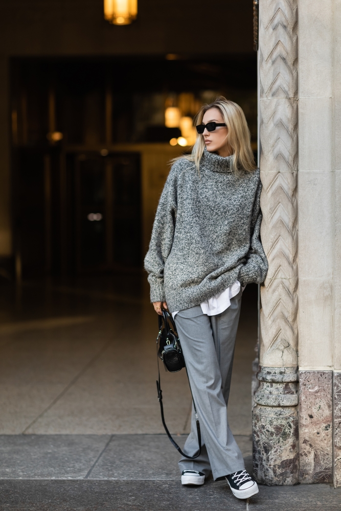 A woman leans against a column in grey pants, a button down shirt, and a fleece turtleneck jacket. She knows what to wear in Italy in winter.