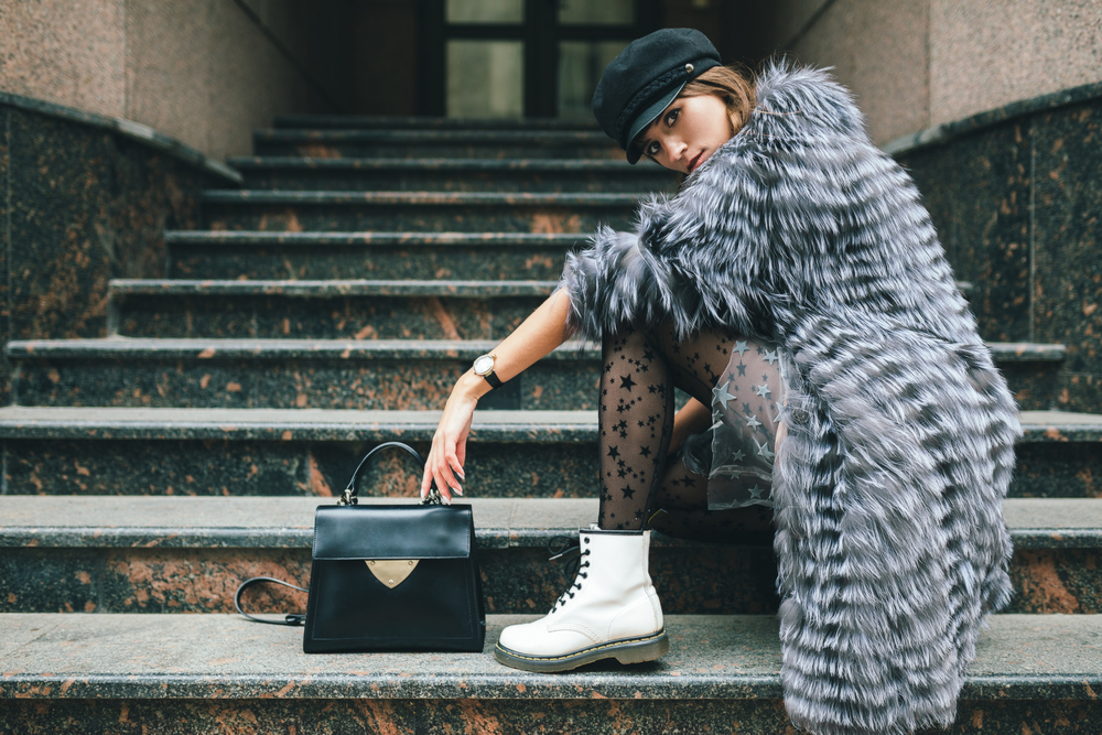 A woman poses on stairs with her structured post, boots, tights, and sherpa long jacket.