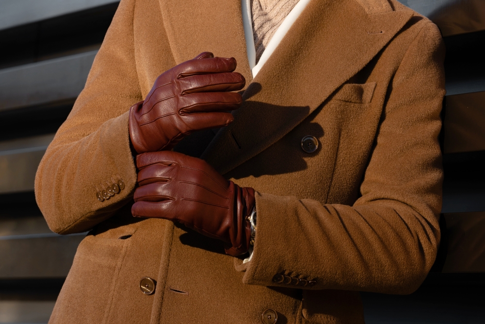 A close up of an outfit shows a wool trench coat and leather gloves.
