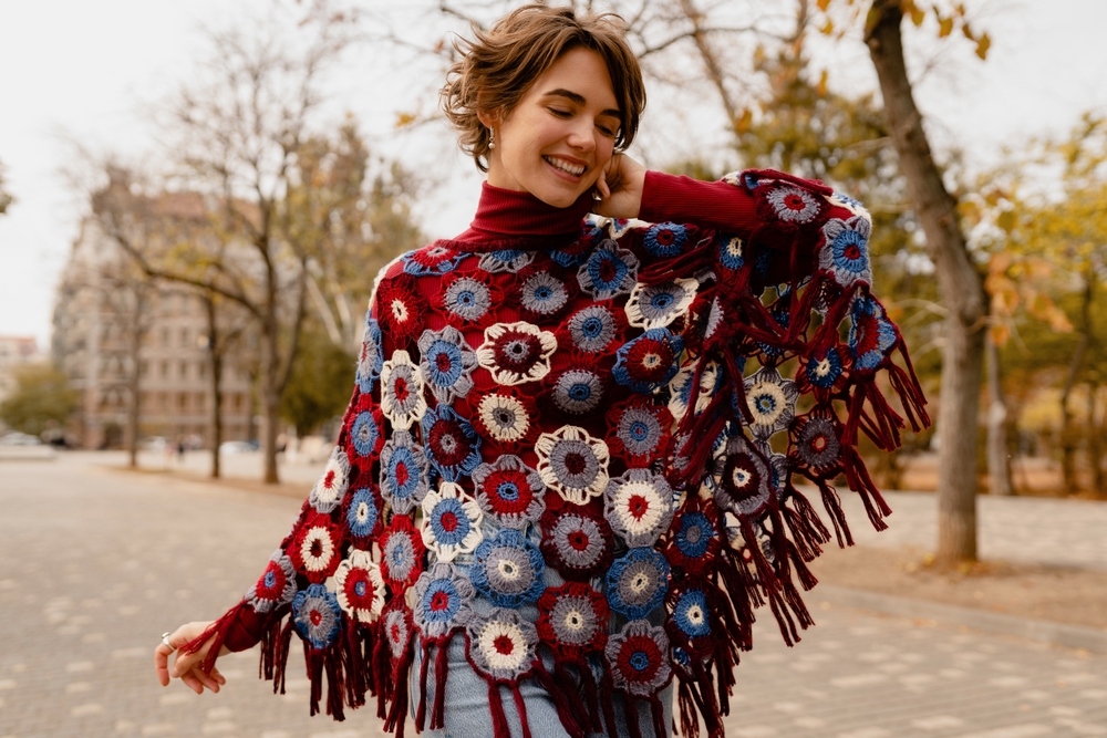 A woman in a knit poncho and turtleneck smiles in the city, knowing What to Wear in Italy in December.