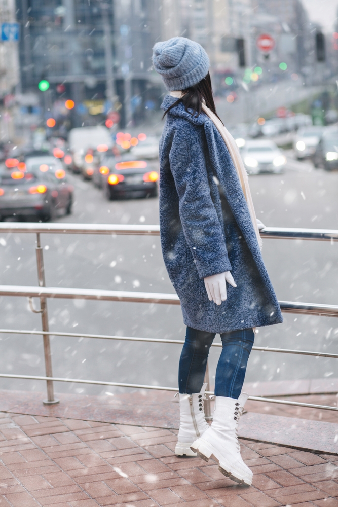 A woman knows What to Wear in Italy in December while wearing jeans, a wool coat, gloves, and a beanie as it snows.