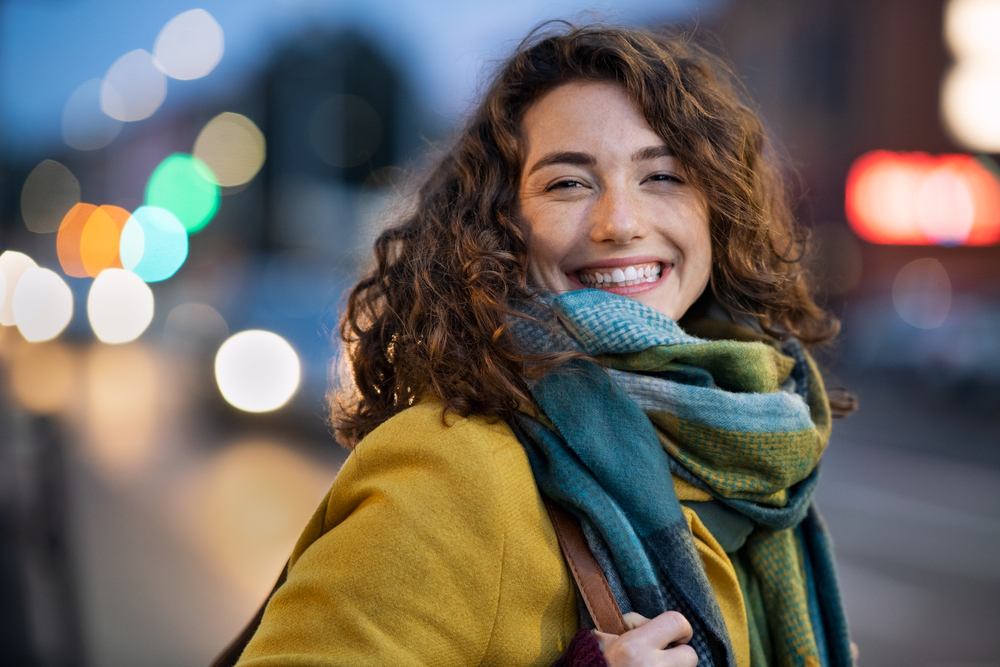 A close up of a woman shows her yellow wool jacket and scarf.