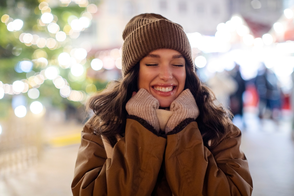 A close up of a girl shows that she knows What to Wear in Italy in December as she clutches her scarf with her gloved hands and wears a brown beanie.
