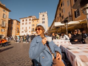 A woman leans back in her chair at an outdoor cafe, wearing a blue jacket and hat, knowing What to Wear in Italy in December to enjoy this outdoor seating.